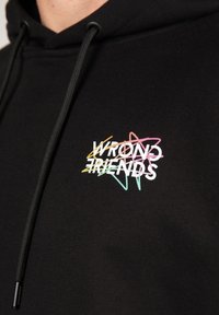 Felpa nera con finitura testurizzata, caratterizzata da un logo multicolore "WRONG FRIENDS" con accenti a forma di stella. Chiusura con coulisse sul cappuccio.