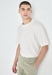 Lys beige kortermet t-skjorte med rund hals, sammen med lysegrønne bukser. Stoffet ser mykt ut med en jevn tekstur.