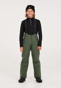 Pantaloni da neve verdi con bretelle nere regolabili, tasche laterali con zip e vita rinforzata, abbinati a un top nero a maniche lunghe e a un berretto nero.