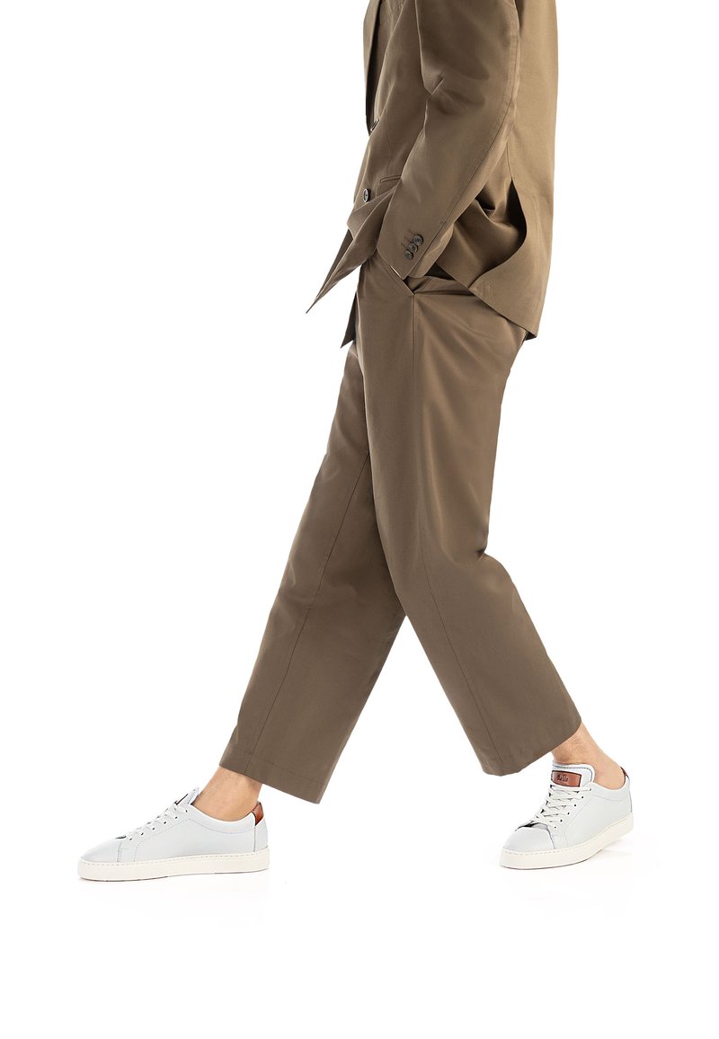 Beżowy garnitur o dopasowanym kroju, połączony z jasnoszarymi sneakersami z skórzanymi akcentami i płaskimi sznurowadłami; model w ruchu.
