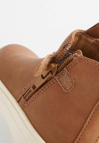 Brune læder slip-on sko med lynlås i siden, struktureret overflade og cremelignende sål. Finesserne inkluderer syede sømme og en stofklap.