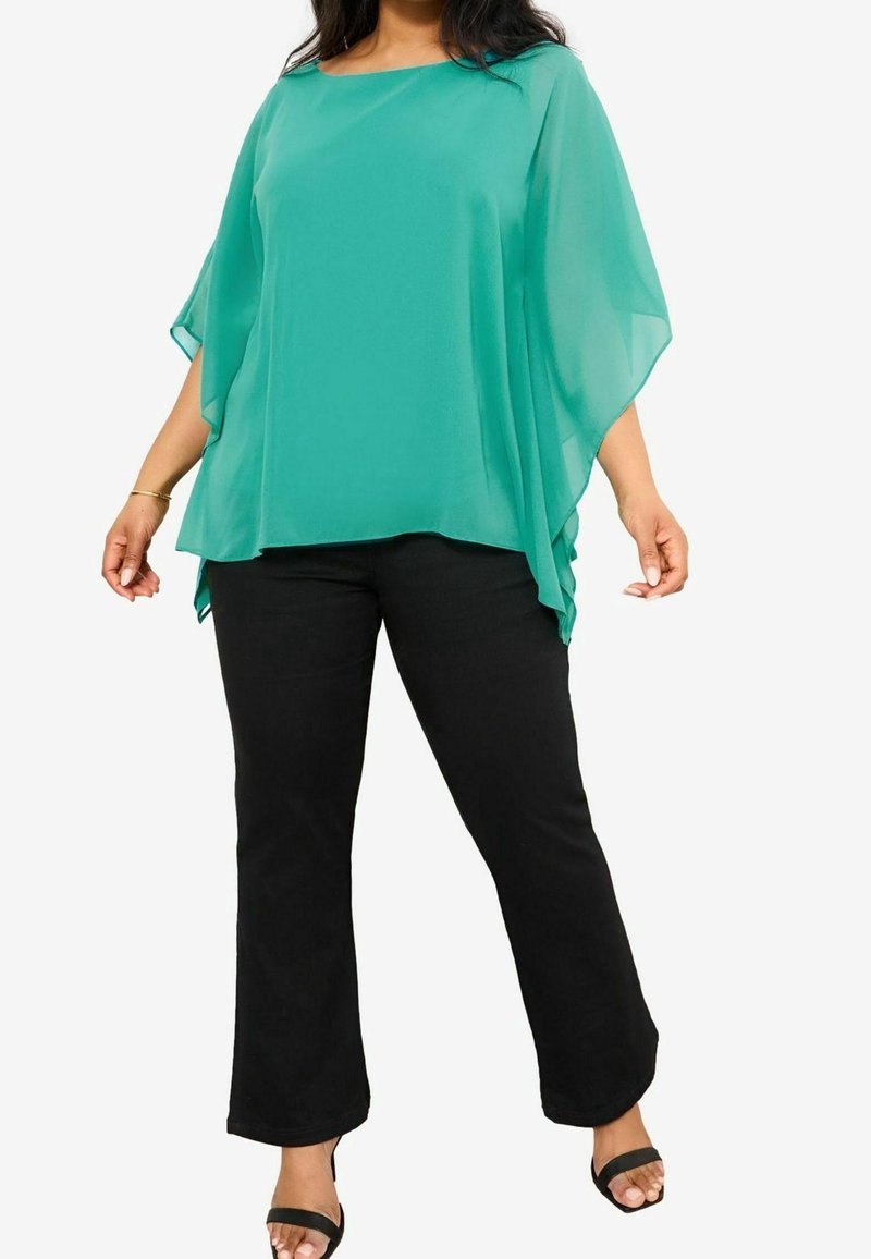 Tunique en chiffon turquoise avec un col carré et des manches larges, associée à un pantalon noir évasé et des sandales noires à brides.