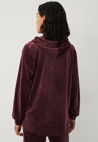 Bordeaux velours hoodie met een relaxte pasvorm, lange mouwen en een verstelbare capuchon. Zachte textuur met een gladde afwerking, minimalistisch ontwerp.
