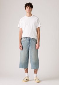 Camiseta blanca de manga corta combinada con culottes de denim azul claro, con un dobladillo deshilachado, y zapatillas beige con acentos amarillos.