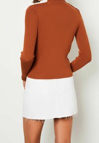 Ribbed, rust-colored knit sweater with a high collar and shoulder button detail, paired with a white denim mini skirt featuring frayed hem.