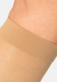 Beige sheer compression sock with a smooth, textured finish and a wide, soft band at the top for comfort.