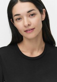 Zwarte, aangesloten t-shirt met een ronde halslijn. Gladde stof met een lichte stretch. Model heeft steil zwart haar en een natuurlijke make-up look.