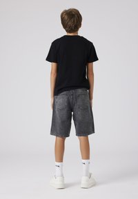 Černé bavlněné tričko, šedé džíny kraťasy a bílé tenisky. Jednoduchý design, volný střih, s zadními kapsami na kraťasech a textem na ponožkách.