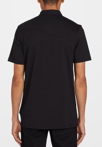 Sort polo t-shirt med vævet krave, korte ærmer og lige kant. Har en subtil sømdetalje på tværs af ryggen. Blødt bomuldsstof.