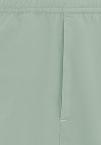 Gros plan sur un tissu vert clair avec une ceinture élastique et une couture verticale visible.