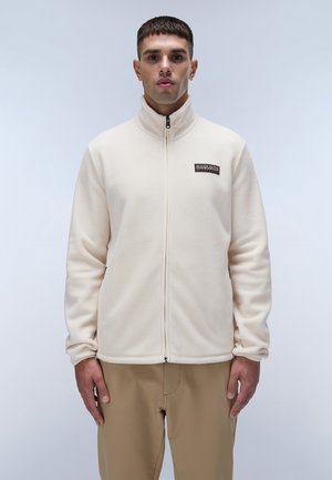 Cream fleece jacket with high collar, full zipper, and a small logo patch at the chest. Smooth texture, fitted silhouette, and long sleeves.