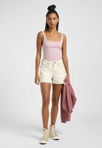 Lyserød ribbet tanktop og hvide denimshorts. Modellen holder en mauve sweatshirt og har cremefarvede høje sneakers på. Simpelt design, afslappet stil.