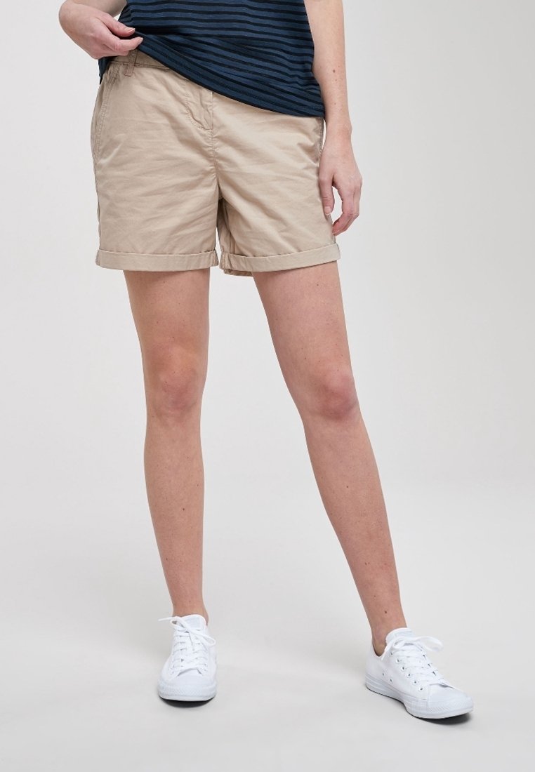 Shorts en coton beige avec revers roulés, dotés de poches latérales, assortis à des baskets blanches. Le haut est bleu marine avec des rayures horizontales.