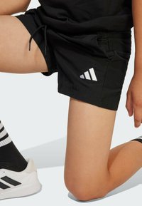 Čierne športové šortky so sťahovacou šnúrkou, s bielym trojuholníkovým logom na ľavom stehne. Hladká látka, dizajn po kolená.