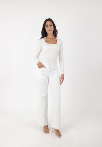 Top de manga larga color crema con escote cuadrado, combinado con jeans blancos de pierna ancha y talle alto, y sandalias de tacón transparente.
