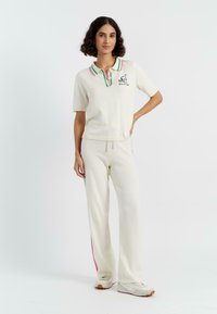 Crème-kleurige co-ord set met een polo met korte mouwen, een multi-gestreepte kraag en geborduurde details, gecombineerd met bijpassende broek met zijstrepen.