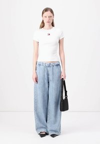 Hvit tettsittende t-skjorte med liten logo, sammen med lyseblå vide denimbukser og en svart håndveske, viser et avslappet hverdagslig utseende.