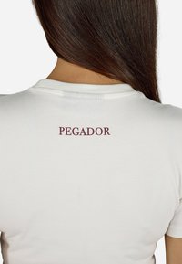 Balts kokvilnas T-krekls ar noapaļotu kakla izgriezumu un īsām piedurknēm, ar "PEGADOR" izdrukātu bordo krāsā augšējā aizmugurē.