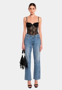 Schwarzer Spitzenbody mit Unterbrustbügel, hellblaue Jeans mit hoher Taille, schwarze Handtasche mit Fransen und schwarze Riemchenabsätze. Glatte Texturen.