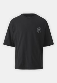 Svart kortärmad T-shirt med en liten vit blommig linjeteckning på vänster bröst, visad mot en enkel ljus bakgrund.