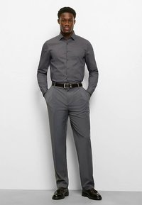 Hemd zum Knöpfen in Dunkelgrau mit kleinem Karomuster, kombiniert mit grauer Hose. Glänzende schwarze Schuhe und ein schwarzer Gürtel runden den Look ab.