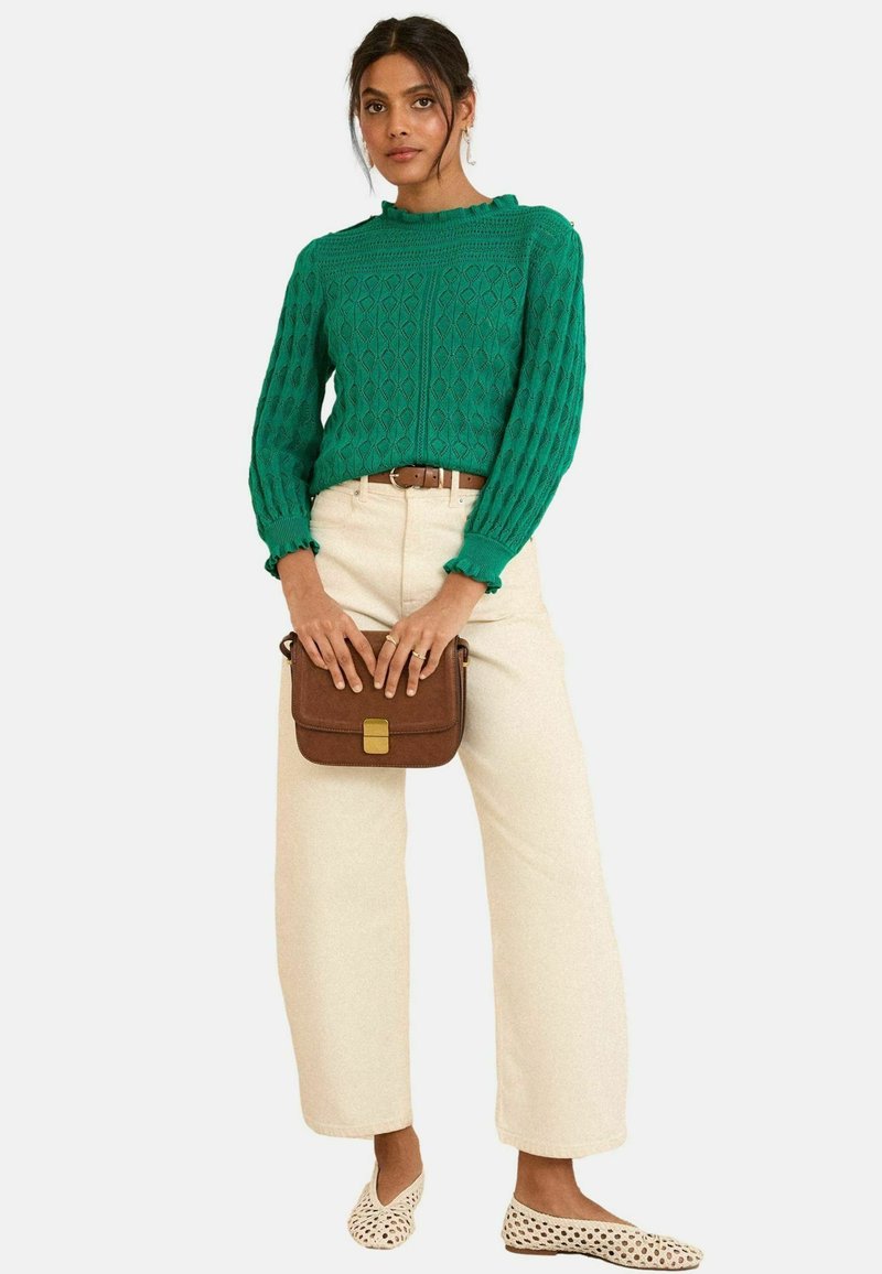 Pull en tricot vert avec des motifs en losange, encolure froncée ; pantalon beige large ; sac bandoulière marron avec fermoir doré ; chaussures claires.