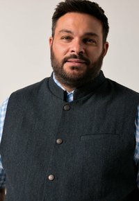 Herre mørk grå vest med et herringbone mønster, med høj krave, fem knapper og en brystlomme, over en lys blå ternet skjorte.