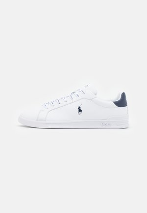 White leather sneakers with a smooth finish, navy accents, and a small logo on the side. Features flat laces and textured rubber sole.