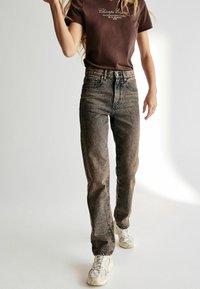 Hög midja, raka jeans i en blekt grå tvätt. Bärs med en brun grafisk t-shirt och vita sneakers, med klassiska sömnadsdetaljer.