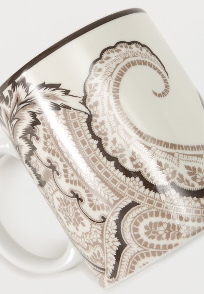 Tasse en céramique blanche ornée de motifs détaillés cachemire et floraux en beige et marron, avec une anse courbée, sur fond blanc.