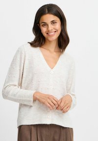 Ljusbeige kofta med V-ringning, strukturerade noppor, ribbad mudd och tre stora knappar fram. Mjuk tygkvalitet.
