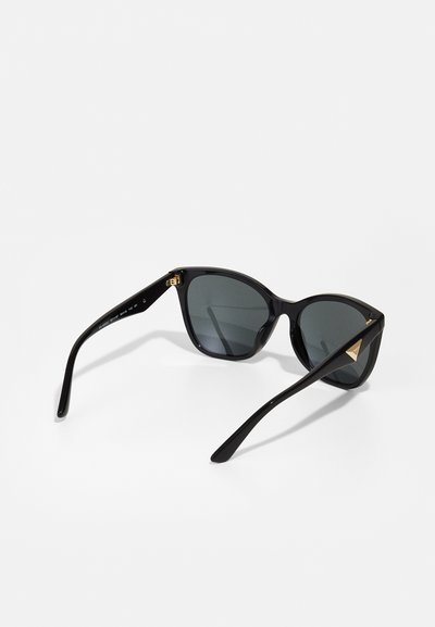 Black sunglasses with a sleek cat-eye shape, dark lenses, and gold accents on the hinges. Temples are glossy with a smooth texture.