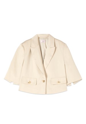 Blazer beige court avec larges revers, manches trois-quarts, deux poches à rabat à l'avant avec boutons dorés, et une fermeture à un seul bouton doré.