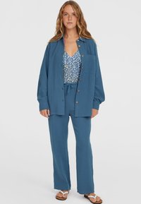 Blauw textuur tweedelig outfit bestaande uit een losse shirt met knopen, bijpassende broek met trekkoord en een patroon top eronder.