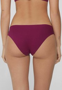 Burgundowe, bezszwowe majtki bikini o średnim stanie. Miękka, elastyczna tkanina dopasowuje się do kształtu ciała, z minimalnym przeszyciem i bez widocznych logo.