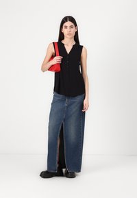 Haut sans manches noir avec un devant boutonné, associé à une jupe maxi en denim taille haute avec une fente à l'avant et des chaussures noires à semelle épaisse. Sac à main rouge.