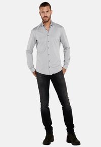 Helles graues Langarmhemd mit Knopfleiste, kombiniert mit dunklen Jeans und schwarzen Schnürstiefeln, in einer taillierten Silhouette.