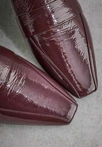 Glossy burgundy patent leather shoes with a pointed toe and a wide strap across the upper, featuring visible stitching and a smooth texture.
