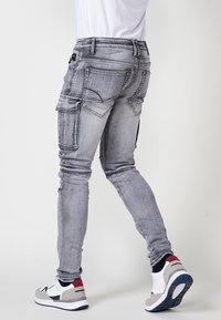 Grijze denim cargobroek met meerdere zakken, slim fit, contrasterende stiksels en een vervaagde afwerking. G gedragen met meerkleurige sportschoenen.