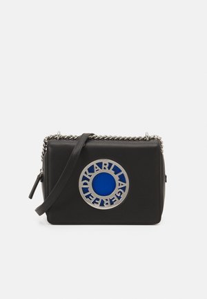 Bolso rectangular de cuero negro con correa de cadena plateada y placa circular con logo plateado y azul en el frente que dice "Karl Lagerfeld".