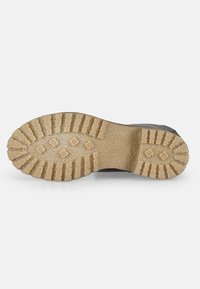 Semelle de chaussure noire avec un profil en caoutchouc beige texturé, présentant de profondes rainures et des motifs circulaires pour une adhérence et une traction optimales.