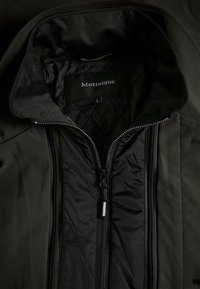 Veste noire avec doublure intérieure matelassée, fermeture éclair frontale partiellement ouverte et étiquette indiquant Matinique taille large au col intérieur.