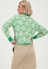 Groen en crèmekleurig gebreid sweater met diamanten motieven, met ribbels aan de groene manchetten en kraag, gedragen met een beige corduroy rok.