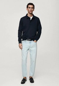 Marinblå långärmad polo skjorta, vit krage, tillsammans med ljusblå jeans och svarta loafers. Enkel design, avslappnad passform och slät textur.