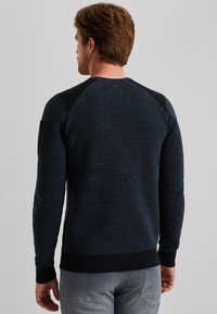 Granatowy sweter dzianinowy o teksturowanej tkaninie, z prążkowanymi mankietami i dołem, czarnymi akcentami na ramionach oraz małą metką z tyłu.