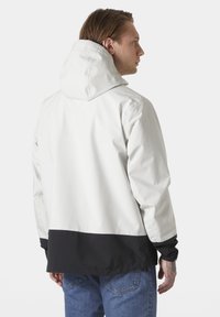 Herrenjacke in Weiß mit einem schwarzen Saum. Sie verfügt über eine Kapuze und elastische Bündchen und besteht aus einem glatten, leichten Material.