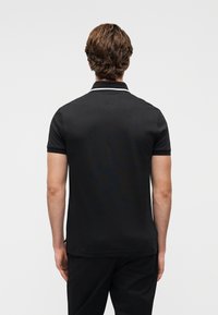 Μαύρο πόλο μπλουζάκι με κοντά μανίκια, με λεπτή λευκή ρίγα στον γιακά και κλασική εφαρμογή. Λ εία υφή, διακριτικός σχεδιασμός.