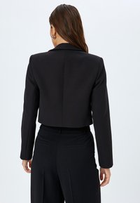 Kurzer schwarzer Blazer aus strukturiertem Stoff, mit Reverskragen, langen Ärmeln und einer glatten Textur in taillierter Passform.