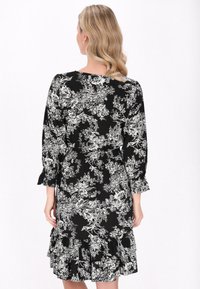Schwarzes Blumenkleid mit langen Ärmeln, rüschigem Saum und tailliertem Schnitt. Verfügt über ein einfarbiges Blumenmuster und eine weiche Stofftextur.