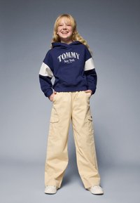 Marineblå hettegenser med "TOMMY New York"-logo og hvite detaljer, kombinert med beige cargo-bukser som har sidelommer og en avslappet passform.